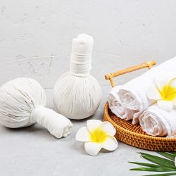 Spa massage Aromatherapy body care background. Spa herbal bags, towel and tropical flowers on gray concrete table. copy space. Beauty and health care concept. High quality photo